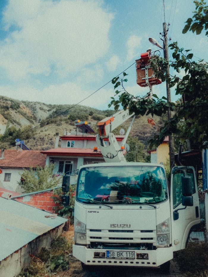 Utility truck with elevated platform repairing power lines in a rural setting.